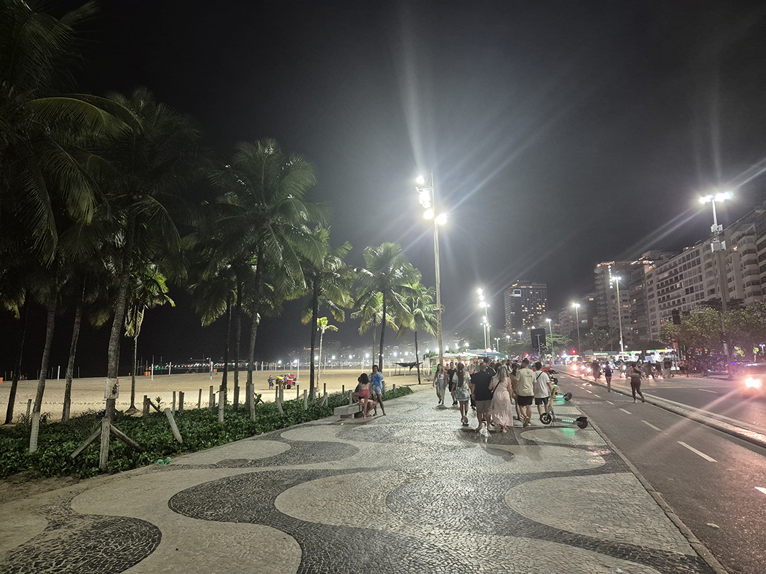Evening atmosphere along Copacabana Beach in Rio de Janeiro, where locals and travelers stroll by the coast, emphasizing the need for caution after dark in major South American cities.
